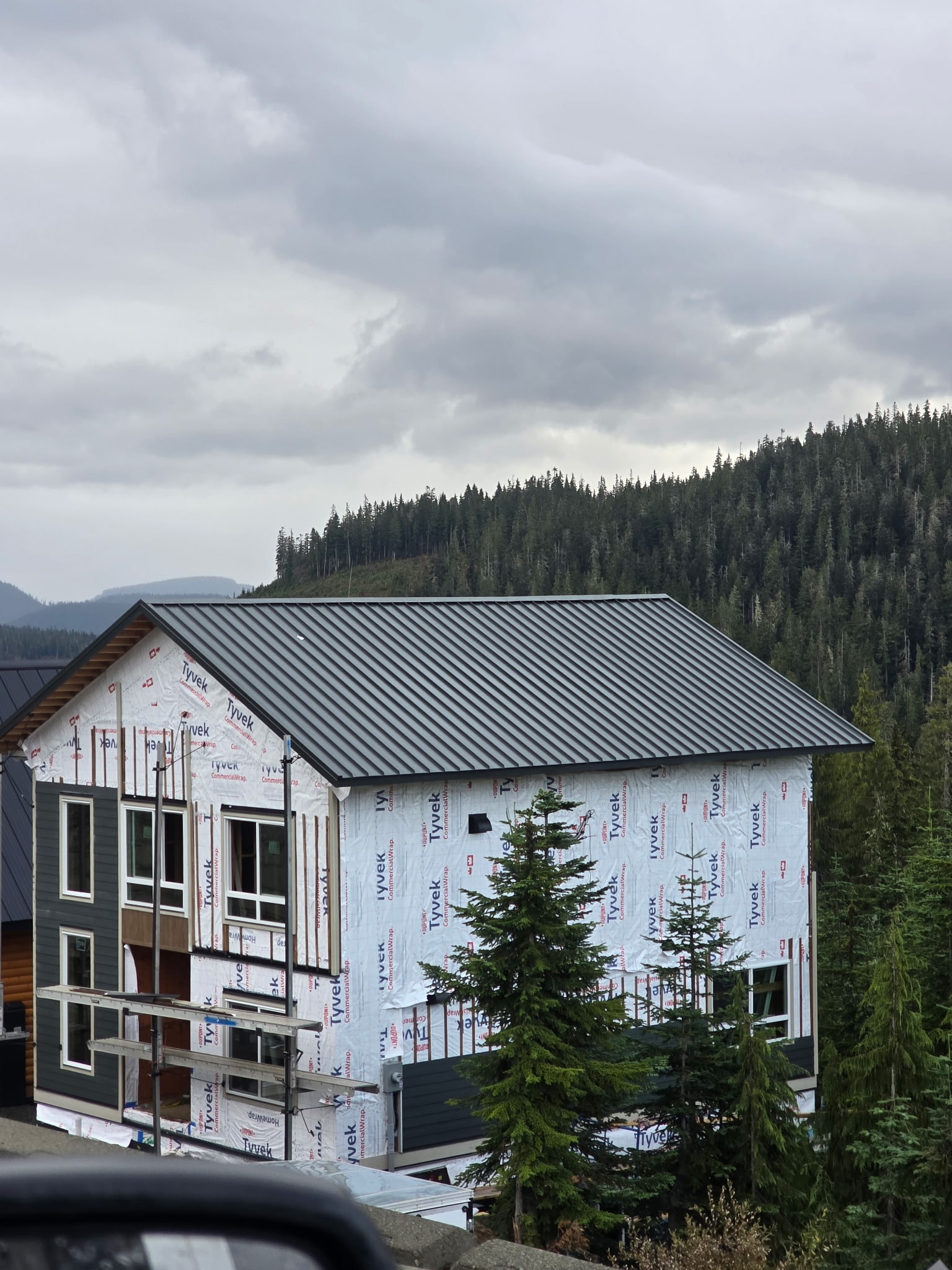 Completed dark standing seam metal roof on mountain home under cloudy sky