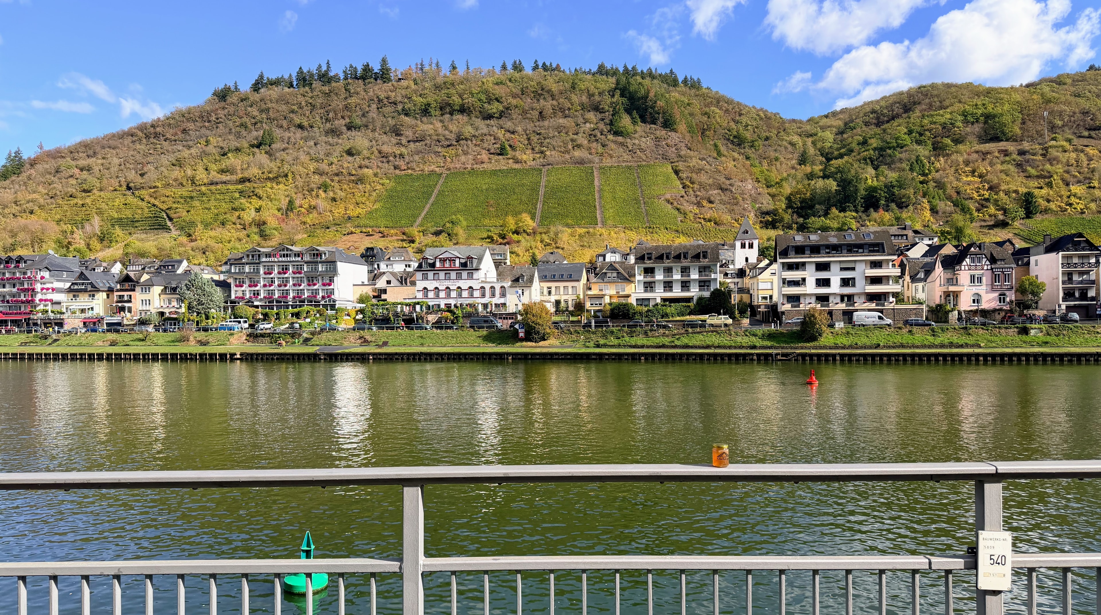 OneKEpp honey jar on a bridge railing over the Moselle River with Cochem town and vineyard hillsides behind
