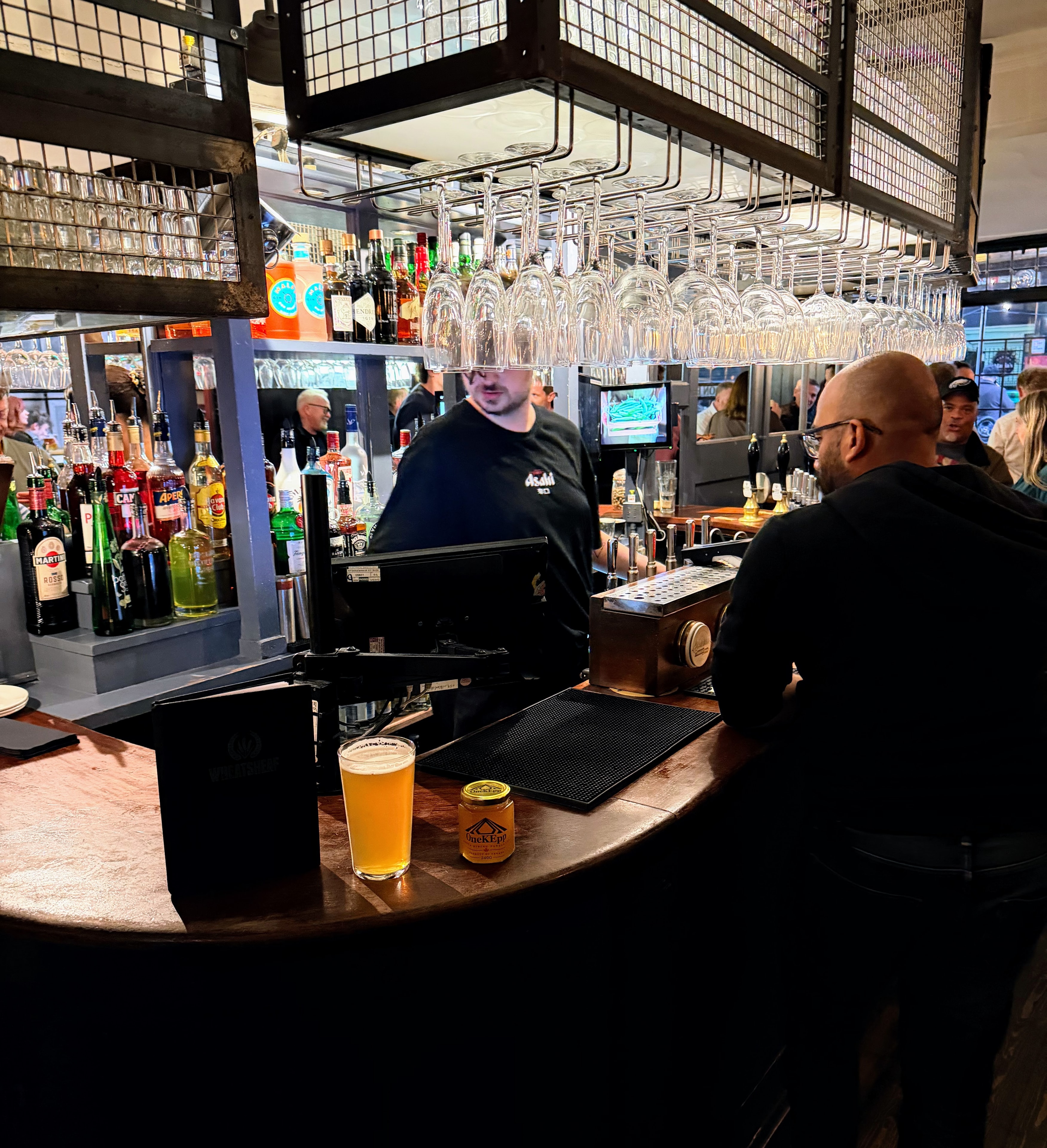 OneKEpp honey jar on the bar at a busy London pub with hanging glassware and spirits